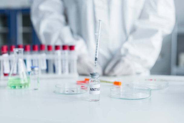 Cropped view of syringe in antigen near blurred petri dishes and scientist in lab  - Φωτογραφία, εικόνα