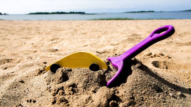 Wooden yellow toy car with toy shovel on sand beach - Foto, immagini