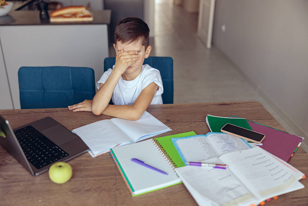 Lazy sad little boy pupil closing his eyes with hand. A lot of difficult homework. Online schooling. - Photo, Image