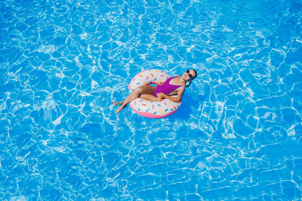 Kaunis hoikka nuori nainen uimapuku nauttia vesipuisto kelluva puhallettava iso rengas kuohuviini sininen uima-allas hymyilee kameralle. Kesäloma. - Valokuva, kuva