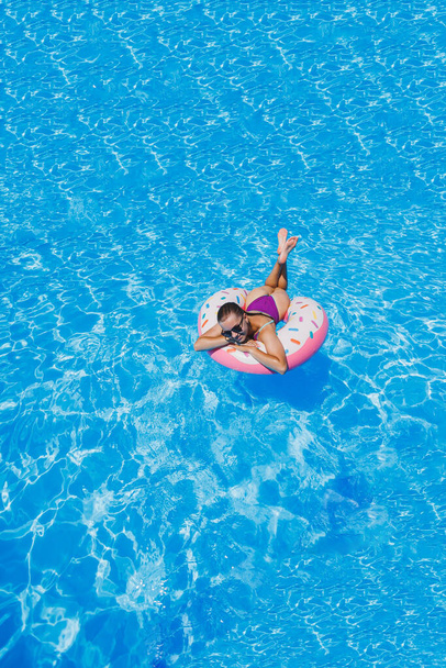 Slanke vrouw met zonnebril in het zwembad in een opblaasbare zwemring in een helder zwempak, zomerfoto, zwemfotografie, zomervrouwenfoto 's. Strand mode - Foto, afbeelding