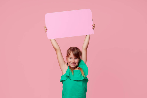 A cute laughing child girl is holding a signboard with an empty space for text. Advertising of childrens products and the announcement of discounts and sales - Фото, зображення