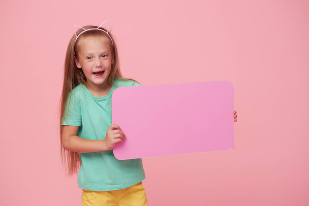 A cute laughing child girl is holding a signboard with an empty space for text. Advertising of childrens products and the announcement of discounts and sales - Photo, Image
