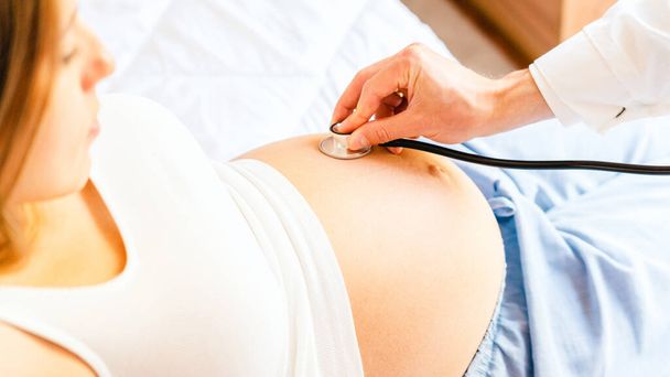 Zwangere vrouw dokter ziekenhuis. Medische kliniek voor zwangerschapsconsulent. Dokter onderzoekt zwangere vrouw buik met stethoscoop. Therapie, gezondheidszorg, moederschap concept - Foto, afbeelding