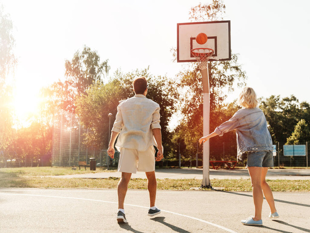 summer holidays, sport and people concept - happy young couple with ball playing on basketball playground - Foto, Bild
