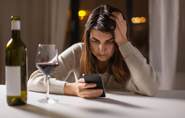 alcoholism, alcohol addiction and people concept - drunk woman or female alcoholic with smartphone drinking red wine at home - Foto, Imagem