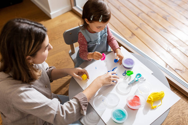 family, creativity and craft concept - mother and little daughter playing with modeling clay at home - 写真・画像