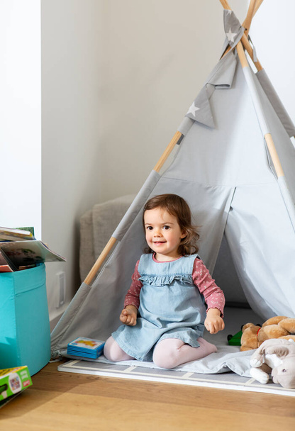 childhood, hygge and people concept - happy little baby girl playing in kids tent or teepee at home - Фото, зображення