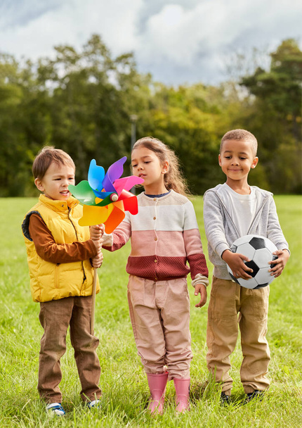 childhood, leisure and people concept - happy kids with pinwheel having fun at park - Фото, зображення