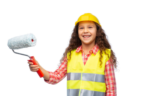 building, construction and profession concept - smiling little girl in protective helmet and safety vest with paint roller over white background - Foto, Bild