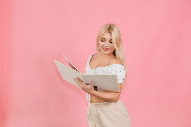 όμορφη κοπέλα με ελαφρά ρούχα με ένα βιβλίο στα χέρια της σε ροζ φόντο - Φωτογραφία, εικόνα