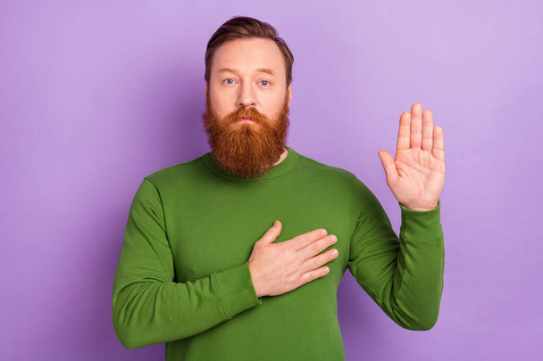 Photo of serious brutal redhead man giving you oath promise touch chest and show palm isolated on violet color background. - Fotografie, Obrázek