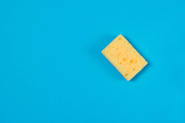 Yellow porous sponge for cleaning and washing dishes on a blue background with copy space. Homework concept - Photo, Image