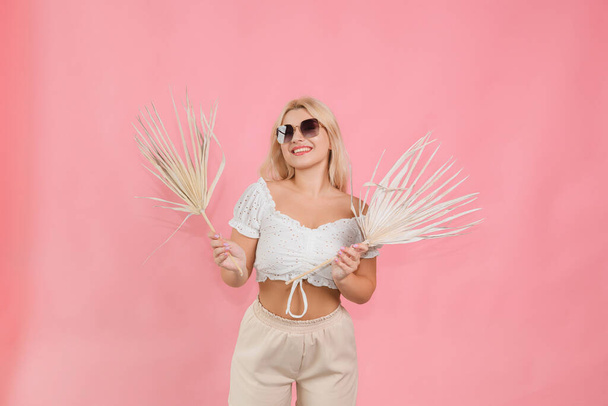 a girl in glasses and light clothes with a plant in her hands on a pink background - Foto, imagen