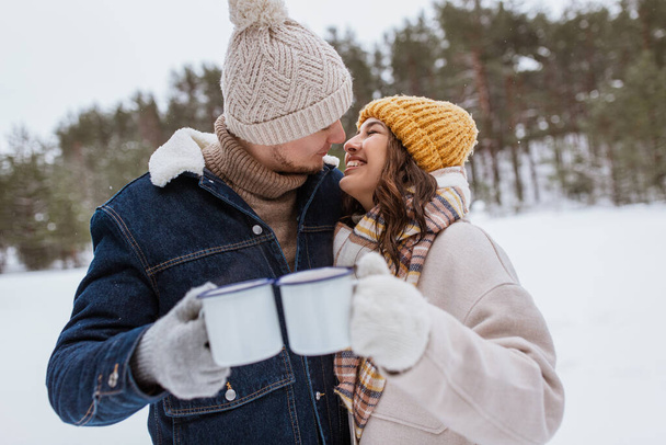 people, season, love, drinks and leisure concept - happy couple with tea cups in snowy winter park - Foto, immagini