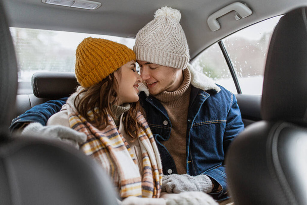 people, love and leisure concept - happy smiling couple hugging and rubbing noses on car back seat in winter - Foto, Bild
