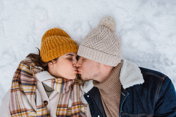 people, love and leisure concept - happy couple kissing lying on snow in winter - Foto, Imagen