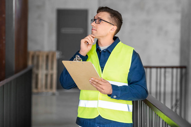 architecture, construction business and building concept - male architect in safety west with clipboard working at office - Foto, imagen