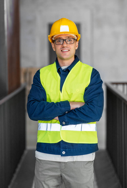 architecture, construction business and building concept - happy smiling male architect in helmet and safety west at office - Foto, Imagen