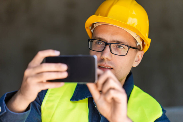 construction business and building concept - male builder in helmet and safety west taking picture with smartphone - Фото, изображение