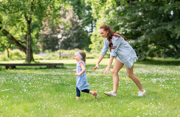 family, motherhood and people concept - happy mother with little daughter playing at summer park or garden - Фото, изображение