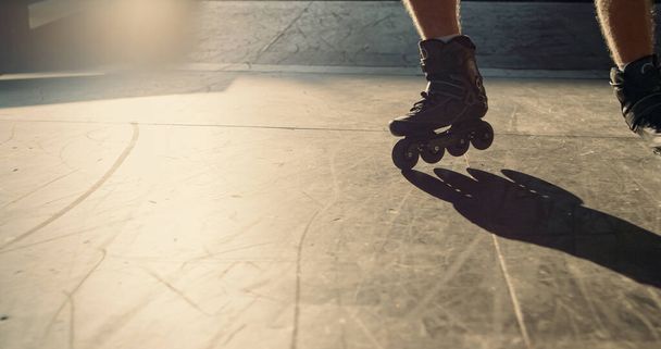 Młody łyżwiarz ćwiczący sztuczki kaskaderskie w skate parku. Zbliżenie nieznanych nóg mężczyzny na wrotkach jeżdżących po nowoczesnym miejskim skateparku. Szkolenia hobby aktywna koncepcja kultury młodzieżowej.  - Zdjęcie, obraz