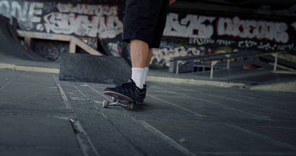 Hombre deportivo haciendo ejercicio en skate board en skatepark. Pies de hombre irreconocibles en zapatillas de deporte montadas en monopatín en la pared de graffiti del parque de skate. Estilo de vida saludable concepto de disfrute del ocio. - Foto, imagen