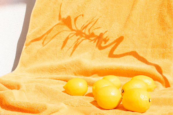 Minimal sunny composition made with lemons and bamboo shadow on an orange beach towel. Contemporary fruit aesthetic. Bright summer background. - Fotó, kép