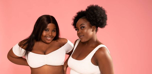 Two beautiful female friends having fun together in studio. Afro women posing on pink pastel background. Real people emotions. Happy lifestyle - Foto, Imagen