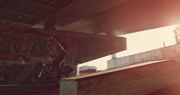 Homens extremos treinando truques no parque de skate moderno com graffiti na parede. Desconhecido bmx piloto e patinador de patins de corrida no espaço urbano. Esporte saudável estilo de vida ativo homens conceito tempo de ação.  - Foto, Imagem