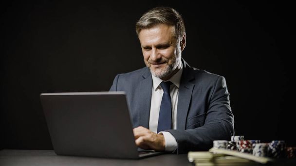 Smiling man in business suit betting online on laptop, playing online poker game - Фото, зображення