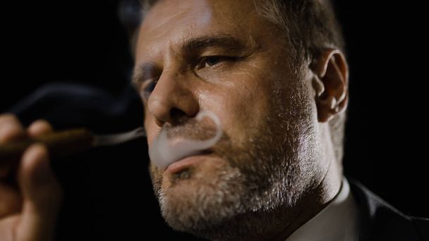 İş elbisesi içinde düşünceli bir adam puro içiyor ve iş stratejisi üzerinde kafa yoruyor. - Fotoğraf, Görsel