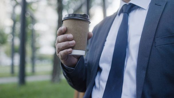 Masculino em terno de negócios bebendo bebida quente no parque, utensílios de papel descartáveis - Foto, Imagem