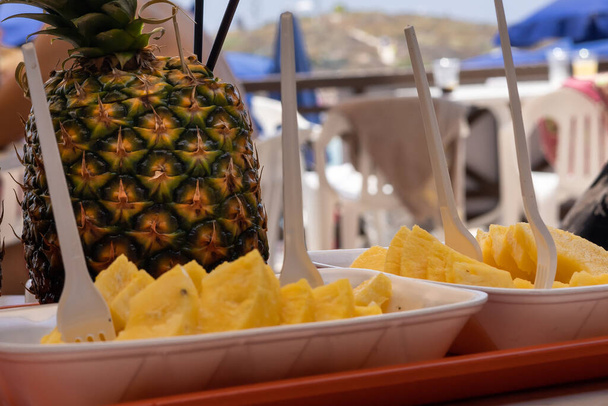 Коктейль пинаколады из свежих фруктов ананаса и ананасовых ломтиков в двух пластинах из пенопласта на пляжном столе.  - Фото, изображение