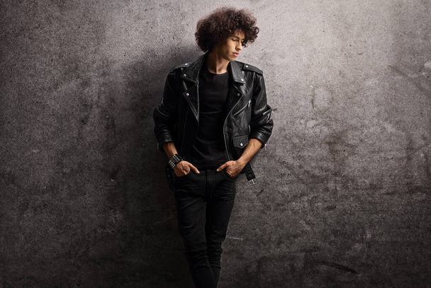Young man in a leather jacket leaning on a gray rugged wall  - Foto, immagini
