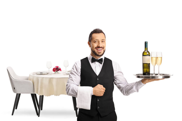 Smiling waiter holding bottle of white wine and glasses on a tray isolated on white background - Foto, Bild