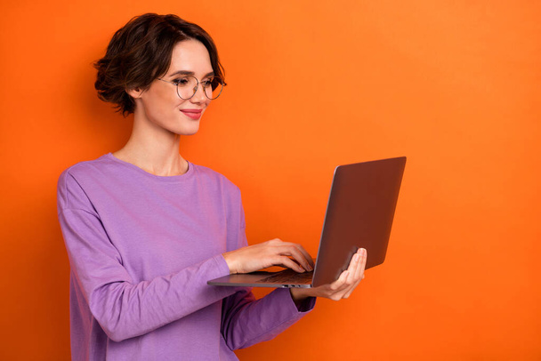 Portrait of smart positive lady hold use wireless netbook write email isolated on orange color background. - Photo, image