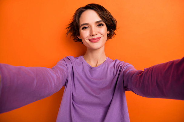 Photo of funny dreamy girl dressed purple pullover recording self video smiling isolated orange color background. - 写真・画像