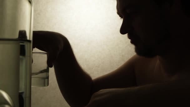 Uomo alcolizzato che beve vodka seduto a un tavolo con bottiglie, video di silhouette - Filmati, video