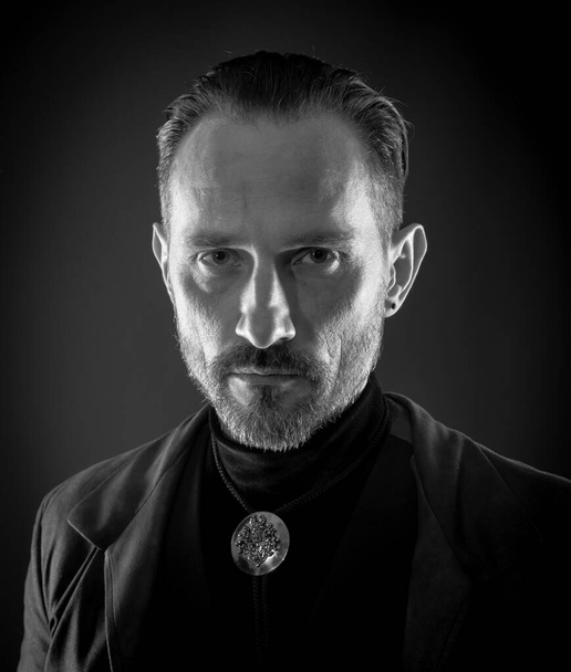 Black-and-white face portrait of courageous handsome man in black coat standing in a dark room. Criminal wild west world, mafia. - Фото, изображение