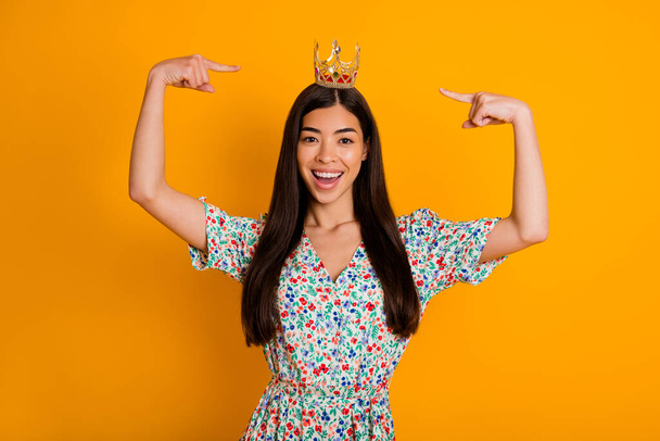 Photo of adorable young selfish female pointing at her beautiful crown on head isolated on yellow color background. - Foto, Imagen