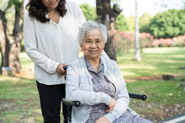 Cuidador de ayudar y cuidar Asiático senior o anciana anciana mujer paciente sentado y feliz en silla de ruedas en el parque, saludable concepto médico fuerte. - Foto, Imagen