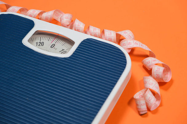 Floor blue scales and centimeter measuring tape on an orange background, top view. The concept of weight loss and weight control. - Photo, Image