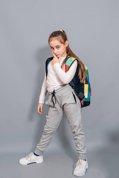 Little girl with backpack. Schoolgirl with backpack looks seriously and frowning. Problems at school. - Φωτογραφία, εικόνα