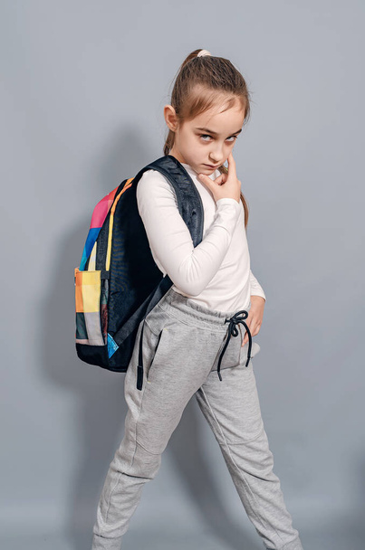 Sırt çantalı küçük kız. Sırt çantalı kız ciddi görünüyor ve kaşlarını çatıyor. Okulda sorunlar. - Fotoğraf, Görsel