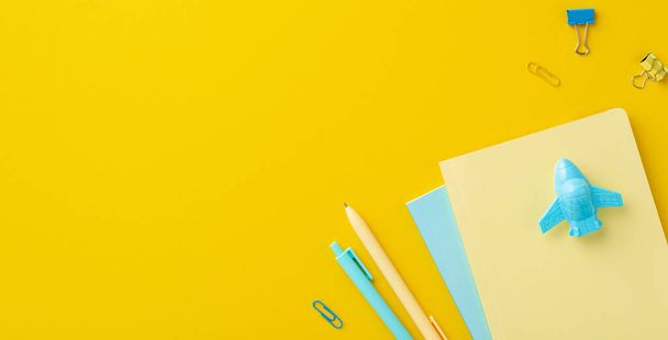 Back to school concept. Top view photo of stationery airplane shaped sharpener over notebooks binder clips and pens on isolated yellow background with copyspace - Photo, Image