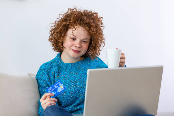 Nuori kaunis nainen onnellinen löytää ostoksia kohteita myytävänä verkossa. Kaunis tyttö käyttää kannettavaa tietokonetta verkko-ostoksia kotona ja juo kahvia - Valokuva, kuva