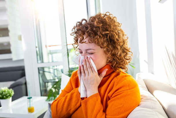 Sick desperate woman has flu. Rhinitis, cold, sickness, allergy concept. Pretty sick woman has runnning nose, rubs nose with handkerchief. Sneezing female. Brunette sneezing in a tissue - Photo, image