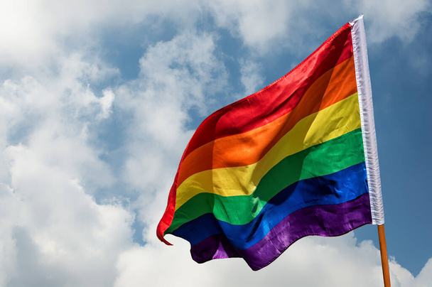 LGBTIQ bayrağı gökkuşağının renkleriyle mavi gökyüzünde bulutlu - Fotoğraf, Görsel