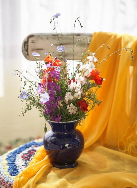 Nature morte avec des fleurs sauvages fraîches dans un vase sur une chaise vintage - Photo, image